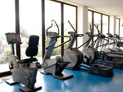 Moderner Fitnessraum mit mehreren Cardiogeräten, großen Fenstern und blauem Boden.