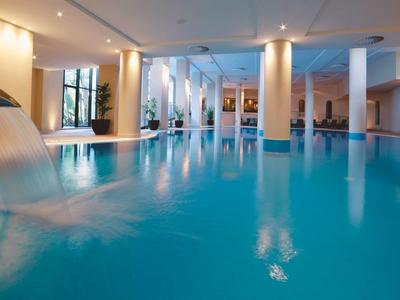 Großer Innenpool mit hellem Blau, Wasserfall, Säulen und gedämpftem Deckenlicht.