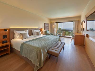 Habitación de hotel luminosa con dos camas, suelo de madera y balcón con vista al mar.