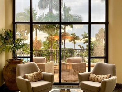 Rincón acogedor con ventana de suelo a techo, vista a palmeras y terraza.