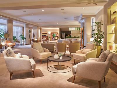 Gemütlicher Hotel-Loungebereich mit bequemen Sesseln, Tischen und warmem Licht.