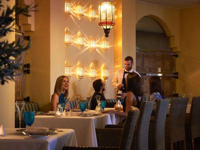 Gemütliches Restaurant mit gedeckten Tischen, Kerzenlicht und einem Kellner im Gespräch mit Gästen.