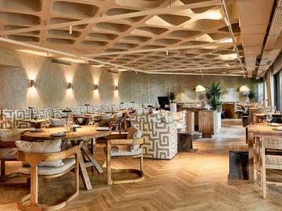 Großes Restaurant mit Holzmöbeln, dekorativen Wänden, hellen Lampen und großem Fensterfrontbereich.