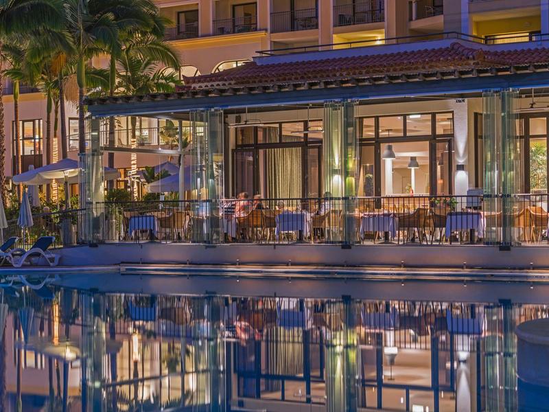 Vista nocturna de un hotel con piscina iluminada y zona de asientos al aire libre.