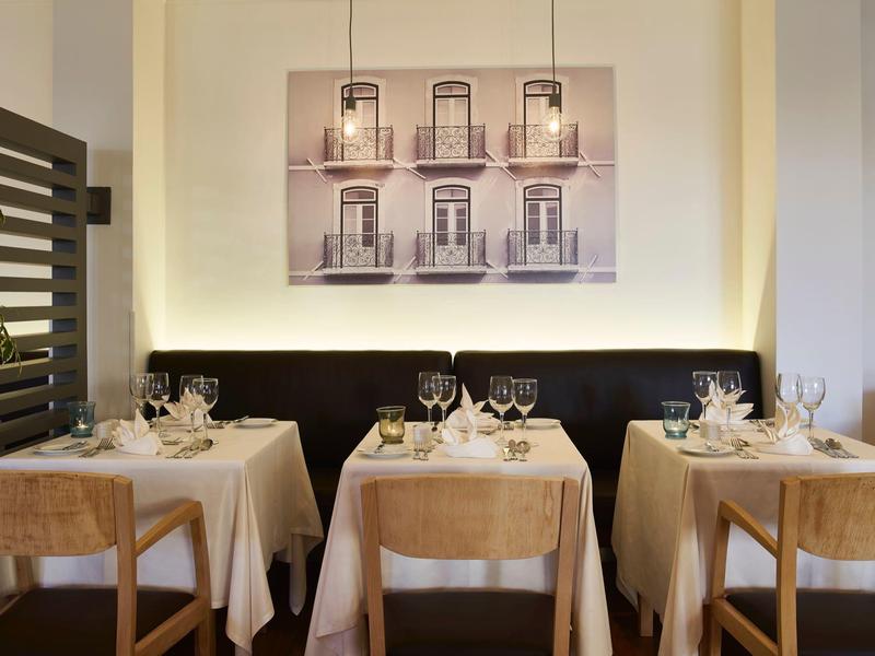 Acogedora zona de lounge de hotel con mesas redondas de madera, sillas y jarrón decorativo con flores secas.