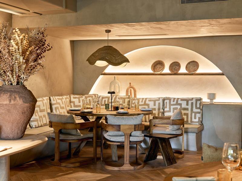 Acogedora zona de lounge de hotel con mesas redondas de madera, sillas y jarrón decorativo con flores secas.