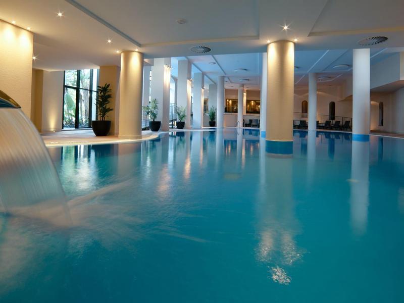 Moderner Innenpool mit Wasserspielen und großen Fenstern in einem luxuriösen Hotel.