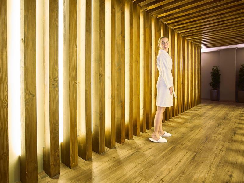 Mujer con bata blanca en pasillo moderno con luces y revestimiento de madera de hotel.