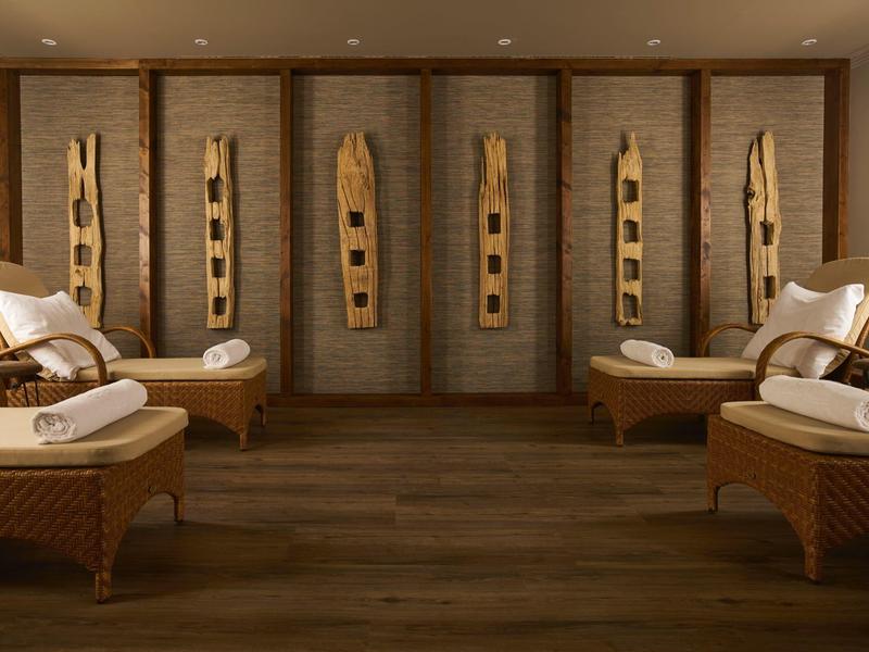 Sala de relajación con camastros de mimbre y elementos decorativos de madera en la pared en el spa.