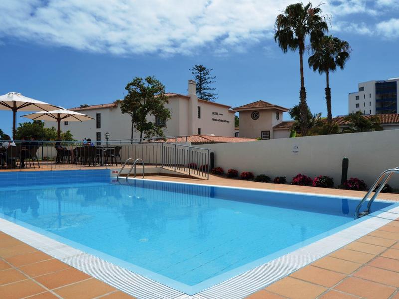 Czysty niebieski basen otoczony terakotowymi płytkami i parasolami pod błękitnym niebem.