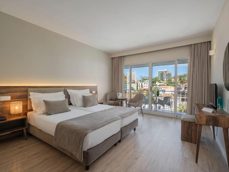 Nowoczesny pokój hotelowy z dwoma łóżkami, balkonem i widokiem na miasto.
