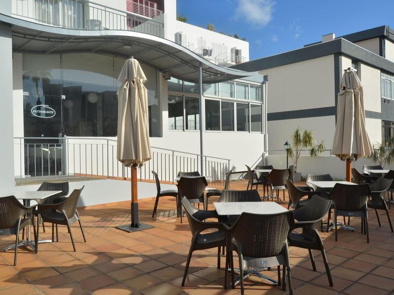 Pusta taras z krzesłami, stołami i zamkniętymi parasolami w słoneczny dzień.