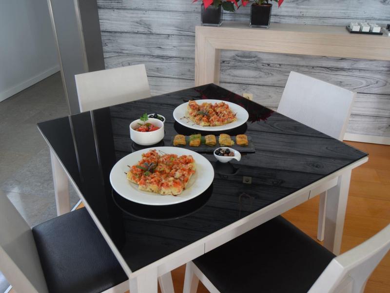 Nowoczesny stół jadalny z czarną powierzchnią, dwa talerze makaronu z sosem pomidorowym i cztery krzesła.
