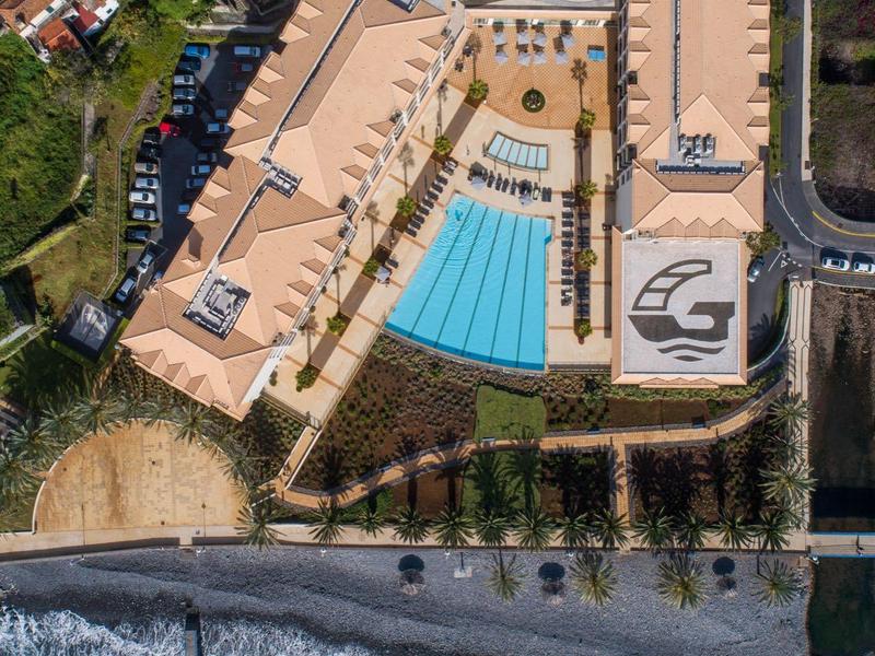 Widok z lotu ptaka na hotel nad brzegiem morza z basenami i zielenią w pobliżu oceanu.