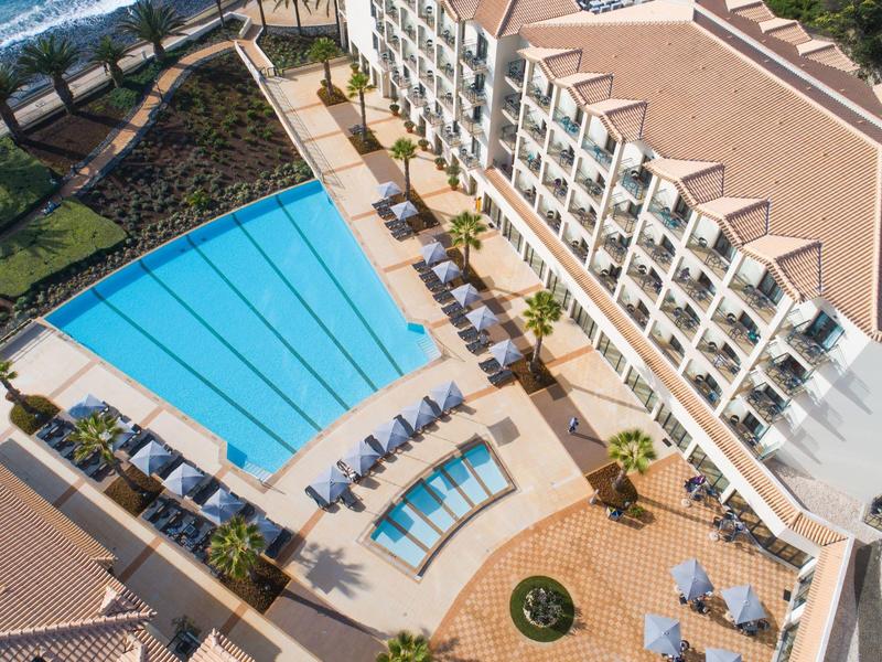 Widok z lotu ptaka na hotel z dużym basenem, mniejszym basenem, leżakami i miejscami do siedzenia na zewnątrz.