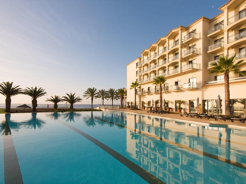 Luksusowy hotel z palmami i basenem infinity o zachodzie słońca.