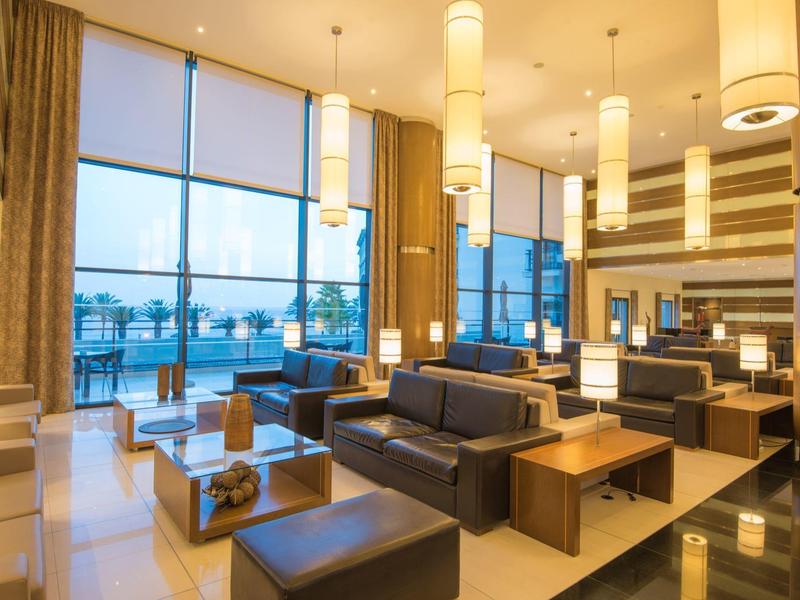 Przestronny hol hotelowy z nowoczesnymi sofami, stolikami i dużymi oknami z widokiem na waterfront.