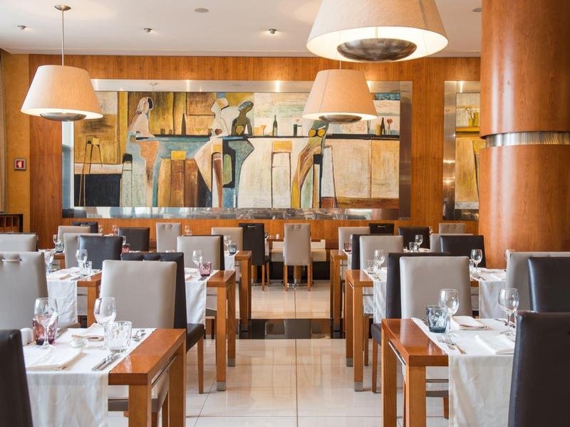 Elegancka restauracja z drewnianymi ścianami, nowoczesnymi lampami wiszącymi i obrazem na tylnej ścianie.