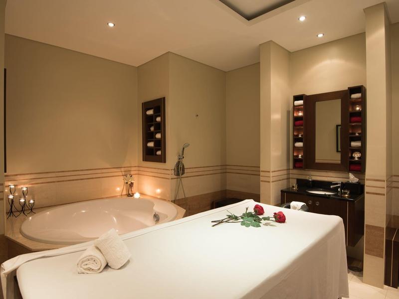 Przytulny pokój spa z łóżkiem do masażu, świecami i wanną przy ciepłym oświetleniu.