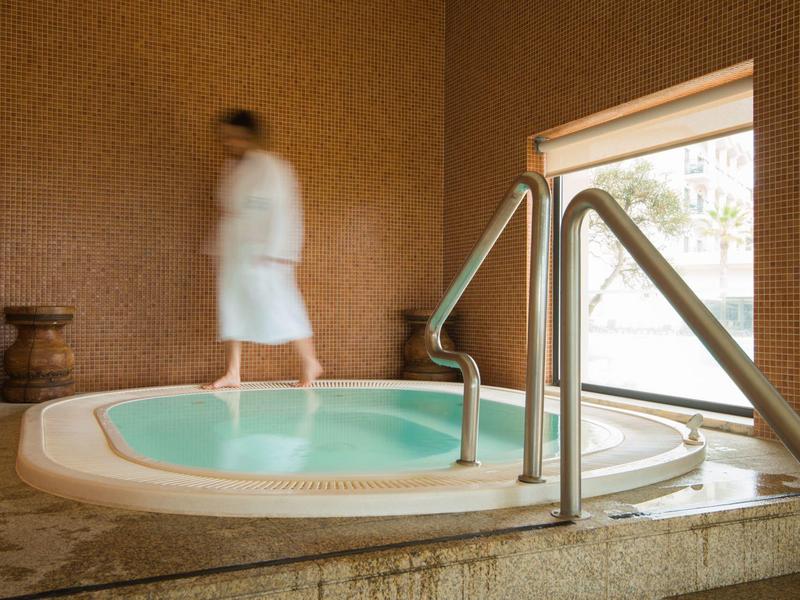 Wanna z hydromasażem wewnątrz z metalową poręczą i osobą w białym szlafroku obok.