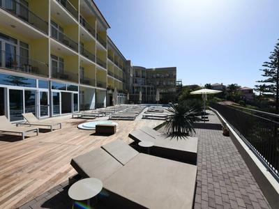 Terrasse ensoleillée avec chaises longues et tables à côté d'un immeuble d'hôtel à plusieurs étages.