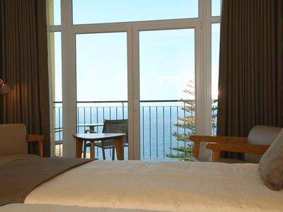 Chambre d'hôtel confortable avec lit, fauteuil et balcon avec vue sur la mer.