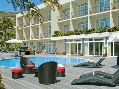 Espace piscine d'hôtel moderne avec mobilier lounge et parasols devant un bâtiment à plusieurs étages.