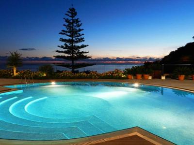 Piscine éclairée au coucher du soleil avec vue sur les arbres et la mer