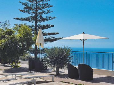 Terrasse ensoleillée avec deux fauteuils, parasols et vue sur la mer bleue.