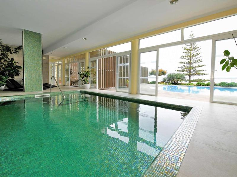 Piscine intérieure avec de grandes fenêtres donnant sur un arbre et un espace extérieur.