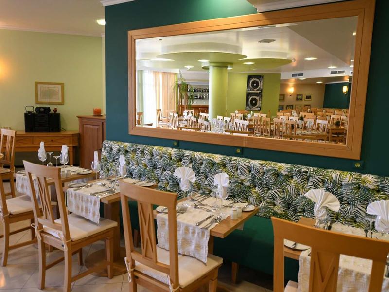 Restaurant avec tables en bois, chaises et un grand miroir sur le mur vert.