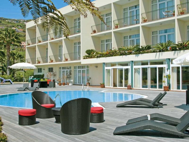 Espace piscine d'hôtel moderne avec mobilier lounge et parasols devant un bâtiment à plusieurs étages.