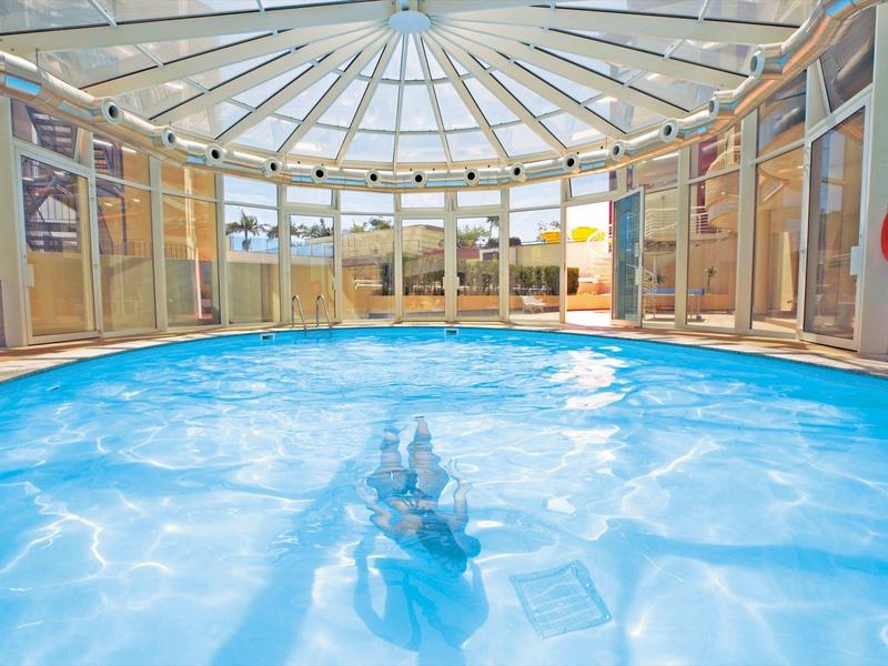 Piscina coperta luminosa con cupola di vetro e area esterna visibile.