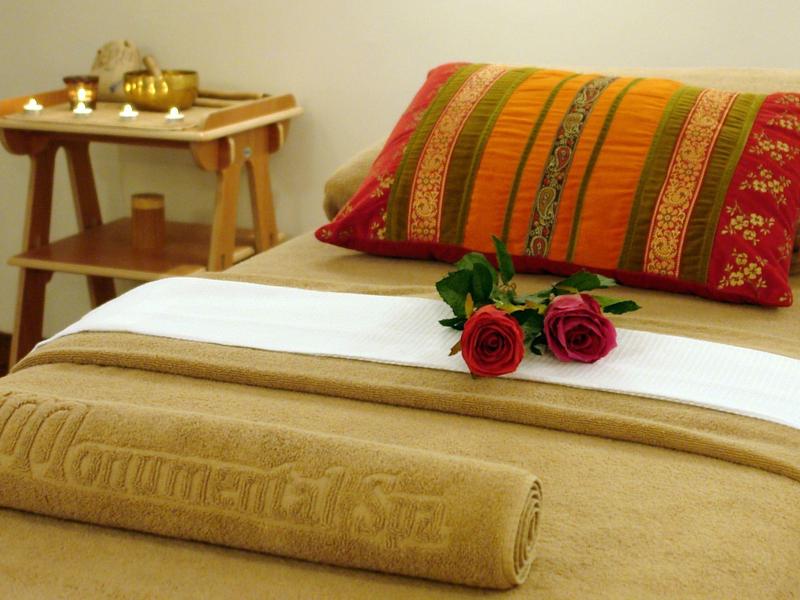 Accogliente letto matrimoniale in hotel con cuscino decorativo e rose rosse su coperta beige.