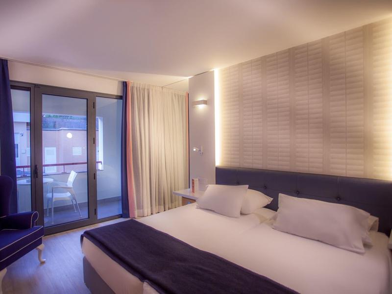 Camera d'hotel moderna con grande letto matrimoniale e accesso al balcone.