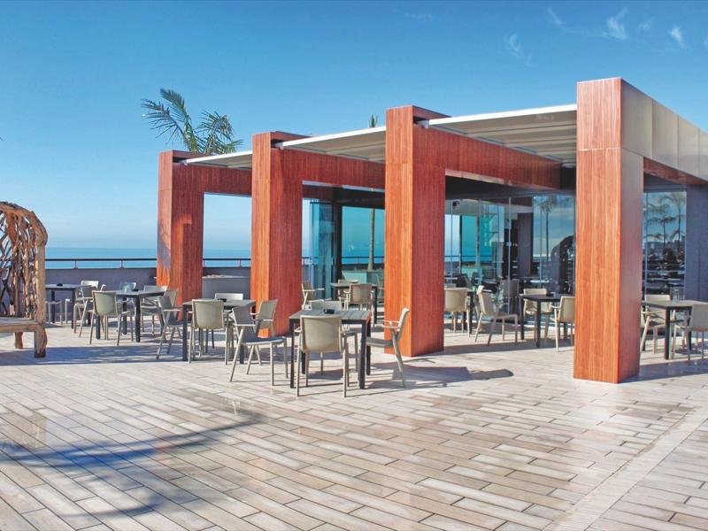 Area terrazza moderna dell'hotel con posti a sedere e vista mare sotto un cielo azzurro.