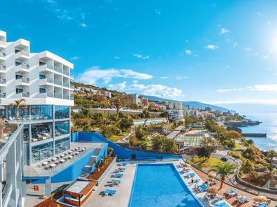 Luxuriöses Hotel mit Pool, Terrassen und Meerblick unter klarem, sonnigem Himmel.