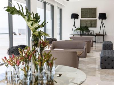 Heller Raum mit Glaswand, modernen Sofas, schwarzen Stehlampen und Tisch mit Blumenarrangement.