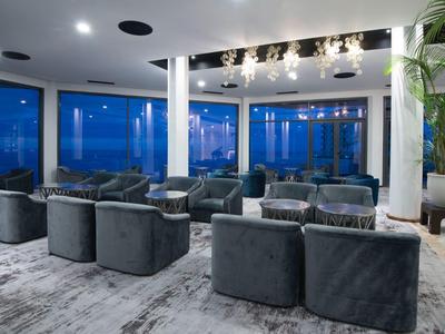 Moderner, heller Lounge-Bereich mit dunkelgrauen Sesseln, großem Teppich und großen Panoramafenstern.