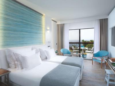 Modern eingerichtetes Hotelzimmer mit Doppelbett, zwei Sesseln und Balkon mit Meerblick.