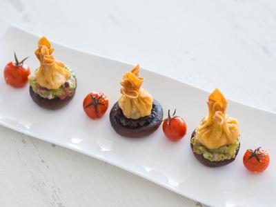 Drei kleine Häppchen mit goldbraunen Teigtaschen auf grünen Blättern, dekoriert mit Kirschtomaten.