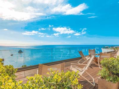 Terras met ligstoelen en glazen balustrade met uitzicht op de blauwe zee en lucht.