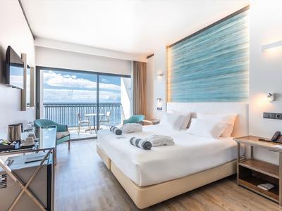 Modernes Hotelzimmer mit Doppelbett, Meerblick, Fernseher, Tisch und Balkon. Hell und einladend gestaltet.