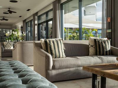 Moderner Wohnraum mit grauem Sofa, gestreiften Kissen und großem Fenster mit Gardinen.