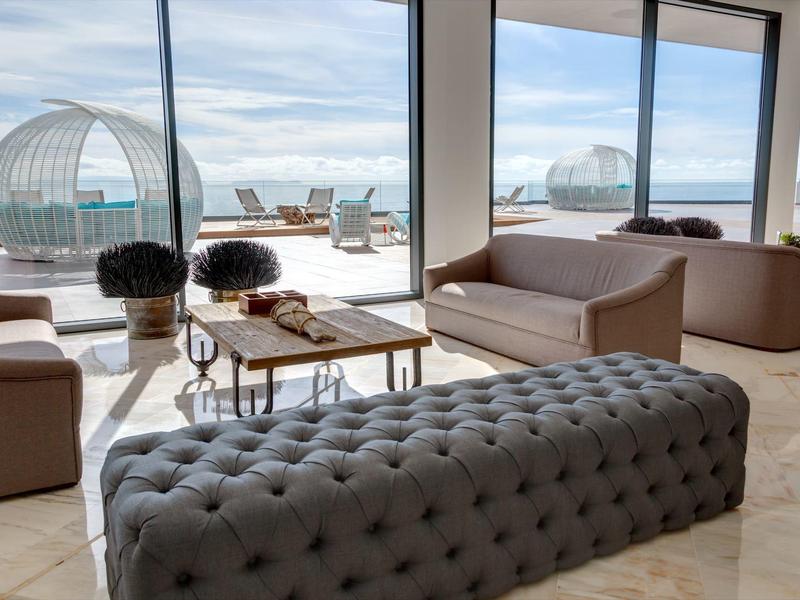 Lichte lounge met comfortabele zitplaatsen en terras met ronde buitenpod's en zeezicht.