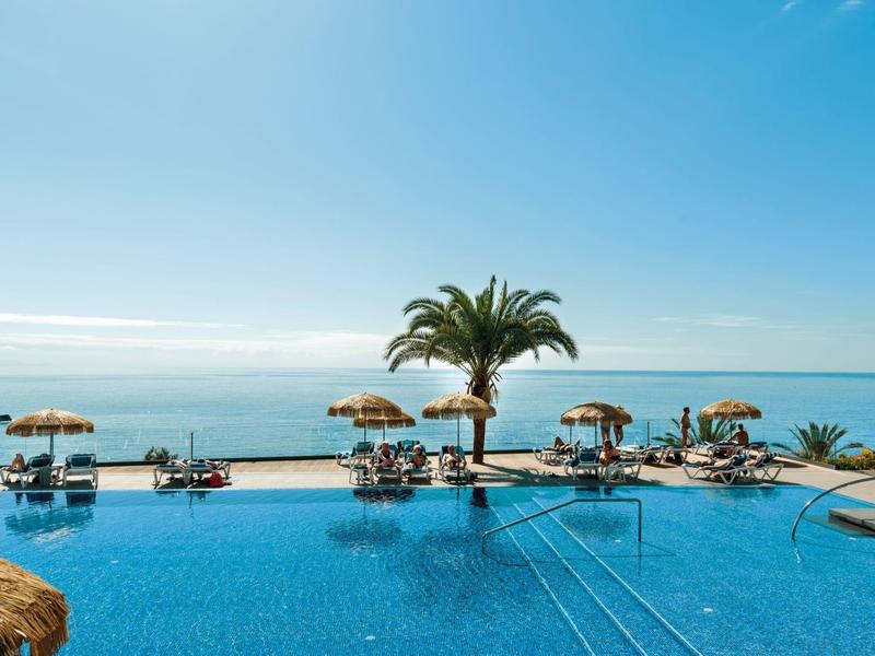 Infinity-zwembad met ligstoelen, palmbomen en zeezicht op een zonnige dag