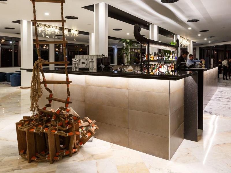 Moderne hotelbar met kubusvormige balie en hangende houten stoel op de voorgrond.