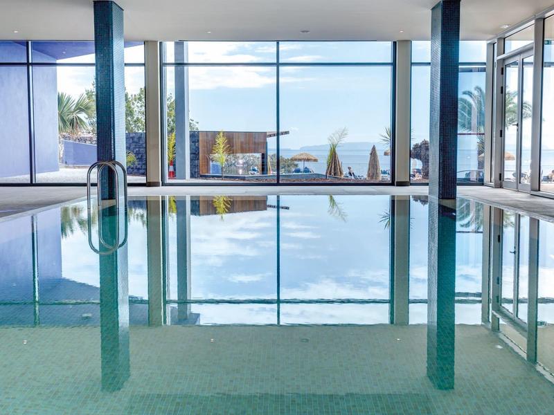 Overdekt zwembad met grote ramen en zeezicht in een modern hotel.
