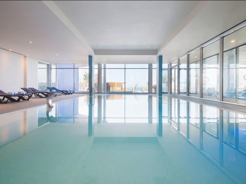 Licht binnenzwembad met glazen wanden en ligstoelen aan de zijkant.