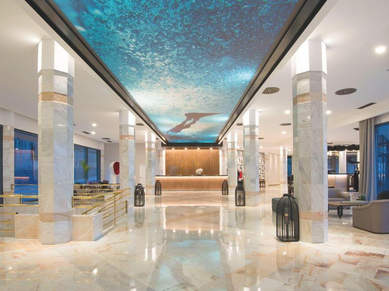 Ruime hotellobby met glanzende marmeren vloer en verlichte blauwe plafondverlichting.